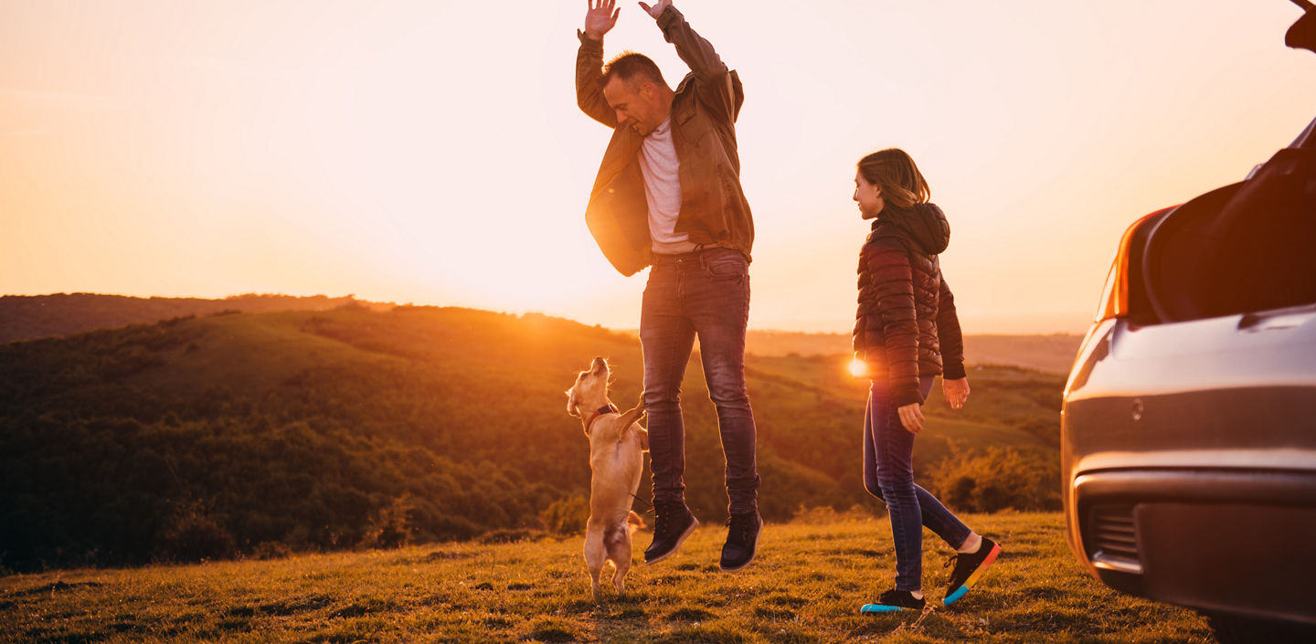 Father and daughter playing with small yellow dog at hill camping during sunset