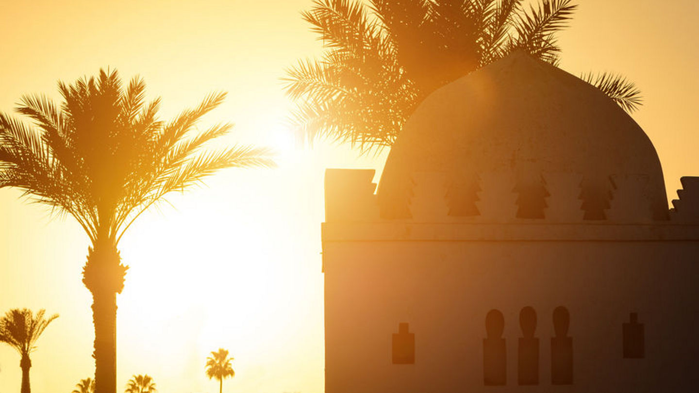 82508056 - beautiful sunset moment with islamic church, palms at background. silhouette of palm trees with old religious building in marrakesh town with gold sun rays and lens flare. wanderlust travel concept.