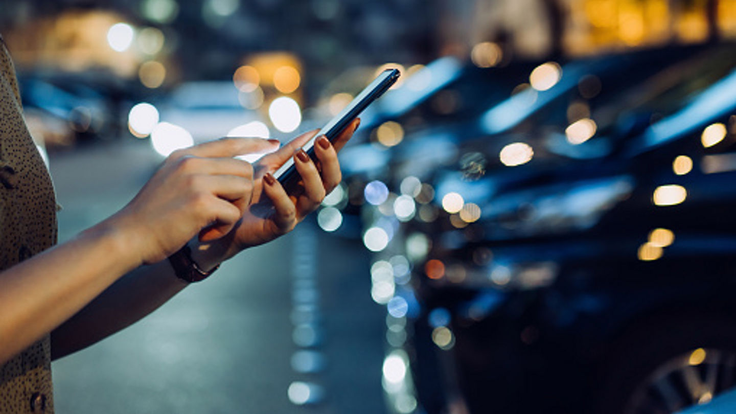 Cropped shot of a woman's hand using smartphone while walking to her car in car park in city at night