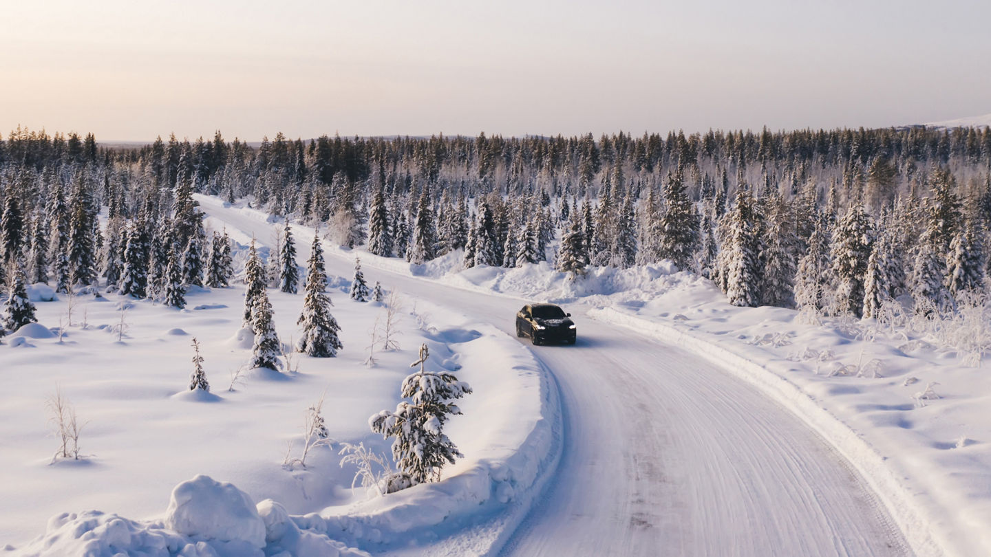 Bird’s eye view of vehicle car moving on rural road having good insurance for winter weather, aerial view of suv automobile driving in scenery area surrounded by coniferous forest