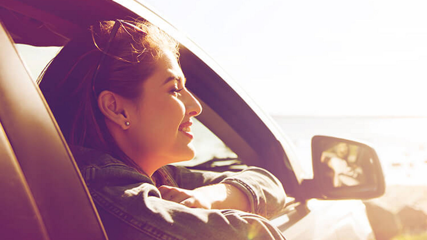 budget-location-lifestyle-young-woman-leaning-out-of-car-window-in-sun-750x750.jpg