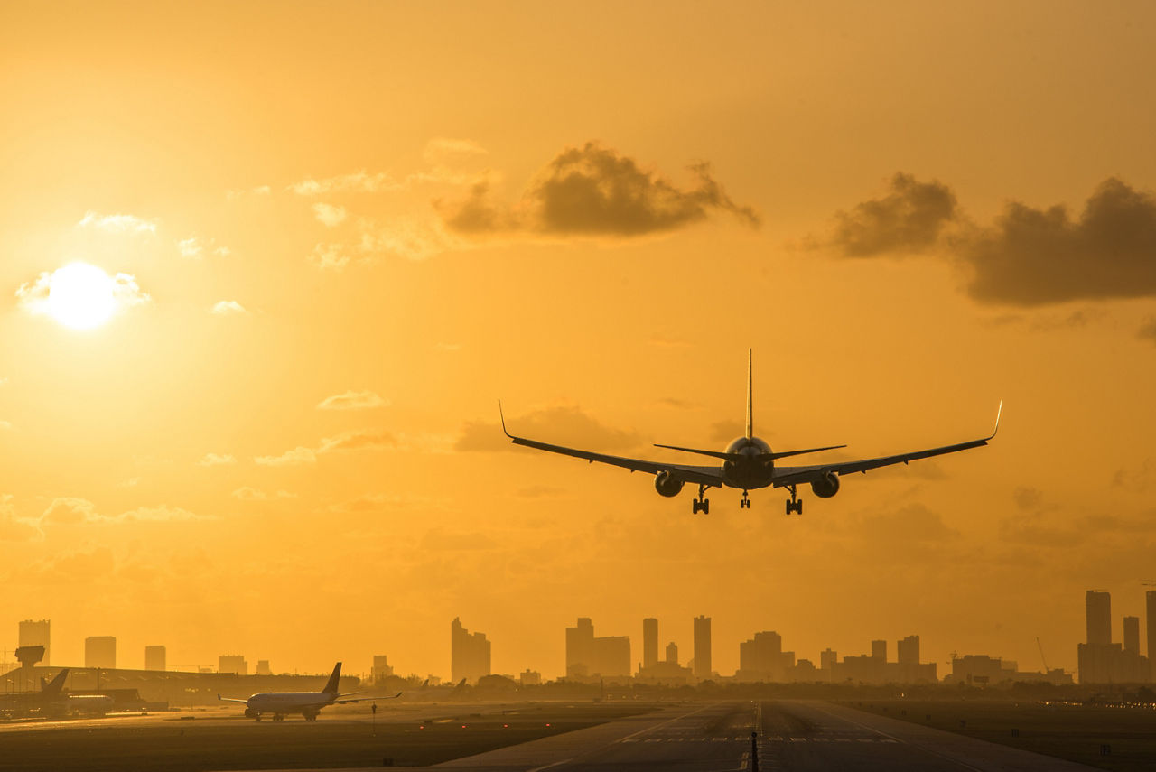Airplane landing at Miami International Airport at sunrise with Miami Downtown skyline in the background.