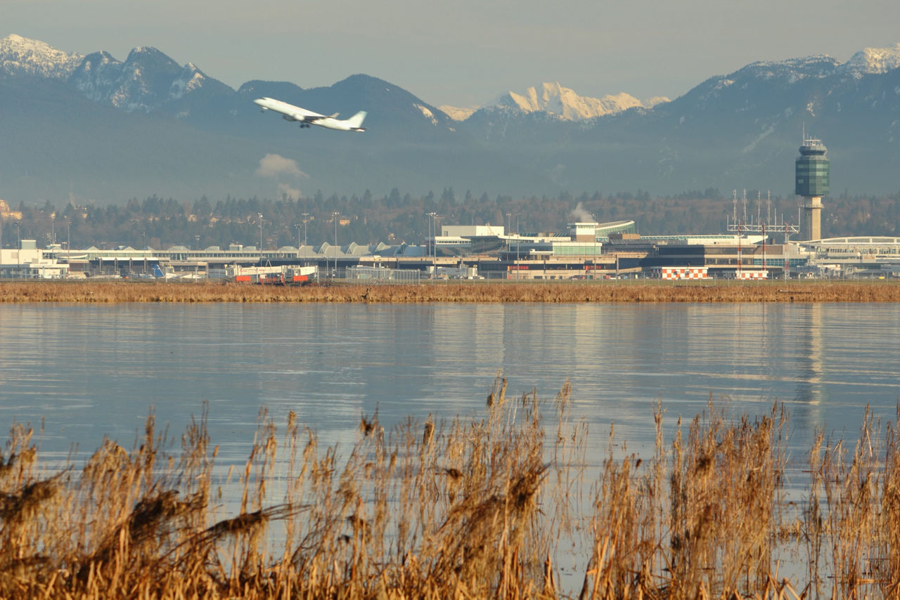 An airplane taking off at Vancouver International Airport, YVR, with the Coast Mountains in the background and the Fraser River in the foreground. British Columbia, Canada.