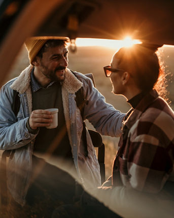 Young couple talking, drinking a coffee watching the sunset from their car.