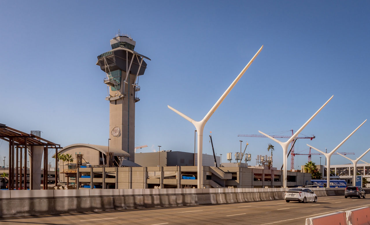 Los Angeles International Airport control tower.  A view of the tower, roadway, odd looking street lights and a few tower cranes in the background.