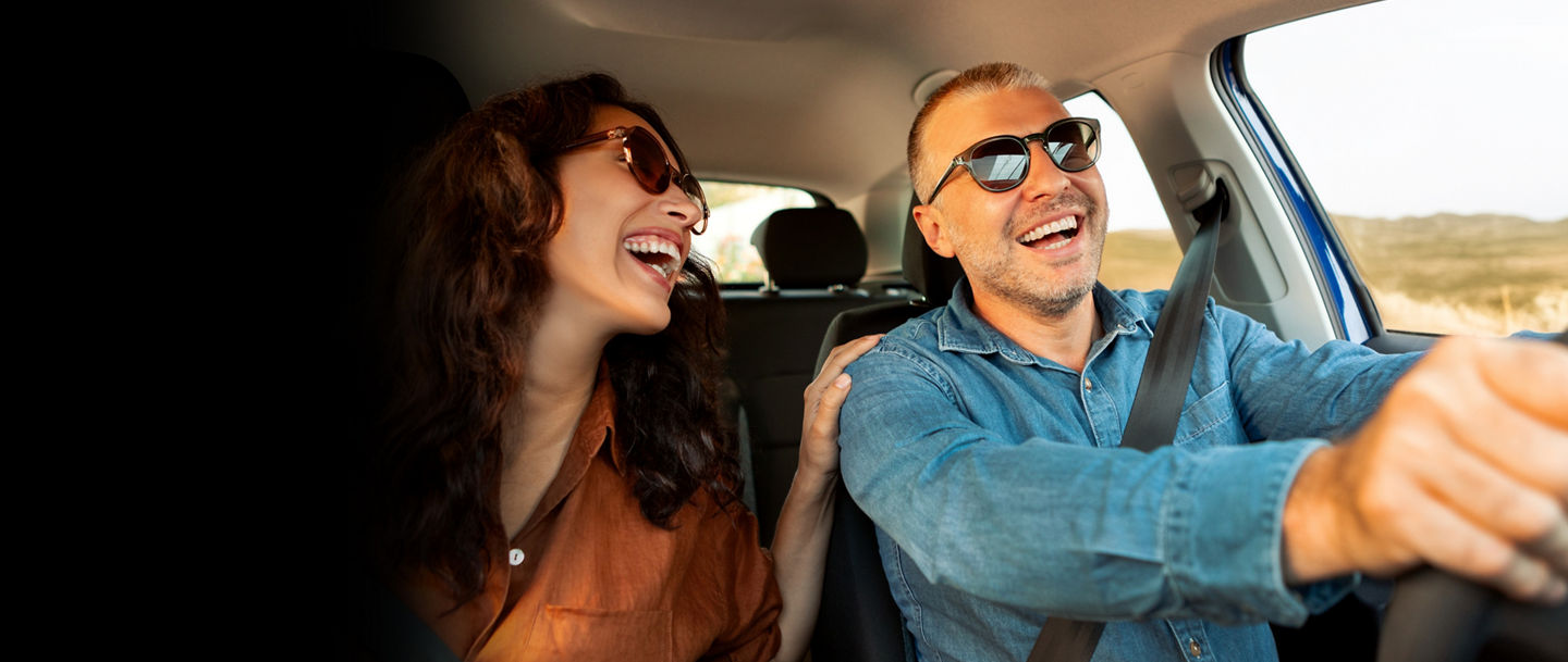 Excited playful European couple in sunglasses driving luxury car, enjoying music, singing and smiling, spouses going on vacation, windshield view